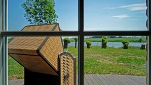 A view through a window of a wooden deck with a built-in seating area, a grassy field, and a body of water in the background. - Holiday Home Rugen-dream (Poseritz)