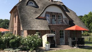 A house with a unique curved roof, a balcony, and a patio area with outdoor furniture. - Holiday Home Rugen-dream (Poseritz)