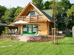 A wooden cabin with a green door, a balcony, and a patio area with outdoor furniture. - The Winkler Family (Neukalen)