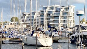 Un port de plaisance où sont amarrés de nombreux voiliers, un bâtiment moderne doté de balcons et un ciel dégagé.