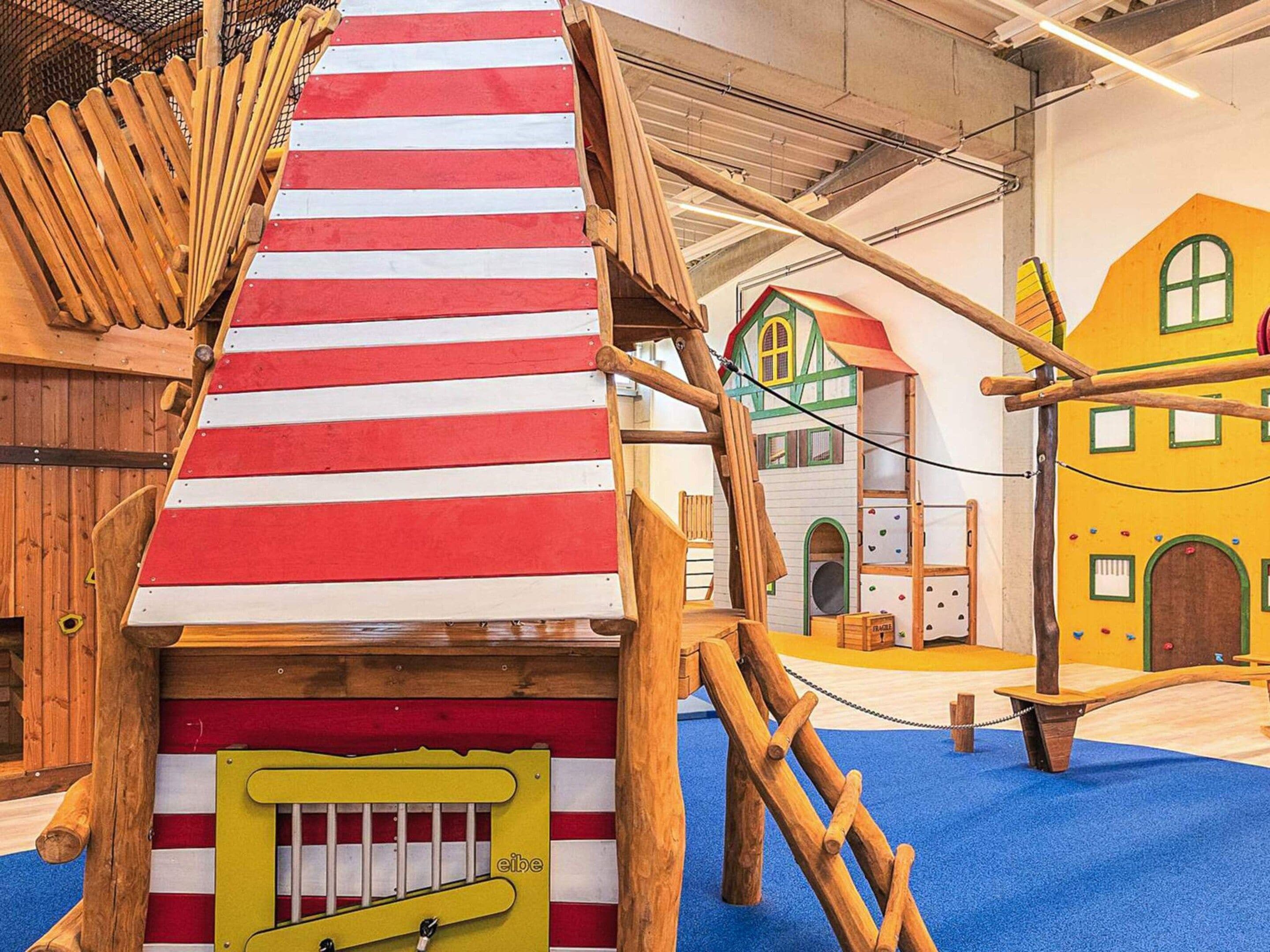 A play structure with a red and white striped roof, wooden climbing elements, and a yellow door.