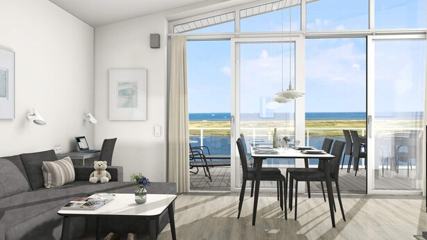 A modern living room with a sofa, coffee table, and a dining area with chairs and a table, all facing large glass doors to a balcony with a view of the beach. - Holiday Home in Wendtorf (Wendtorf)