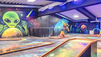 Un espacio interior con un mural de un extraterrestre y planetas, una rampa con suelo temático del espacio, y una estructura circular.