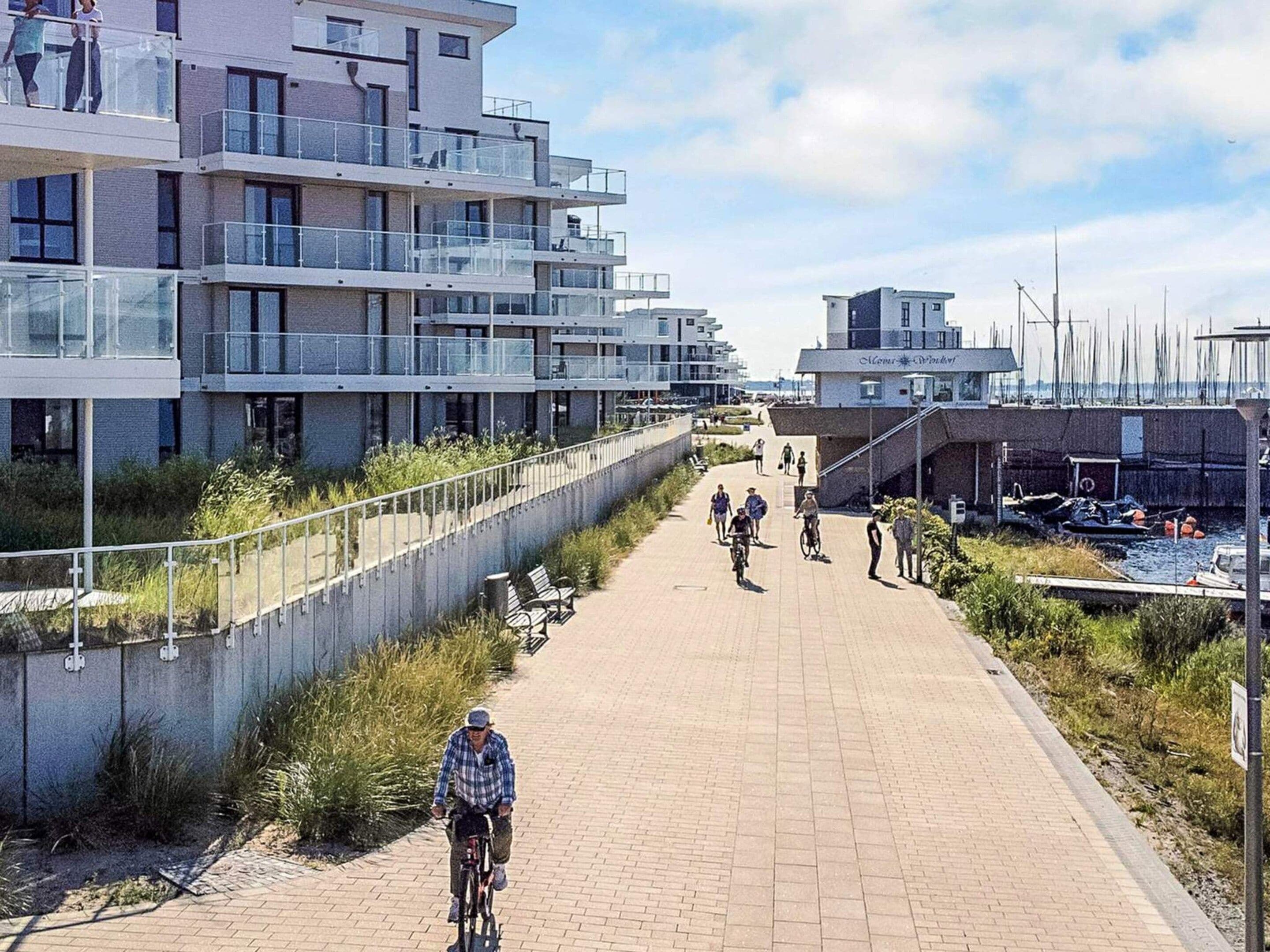 Un passeig pavimentat amb una barana que porta a un edifici modern amb balcons.