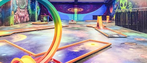 An indoor space with a futuristic design, featuring a large circular structure, a mural with space-themed artwork, and a floor with geometric patterns.