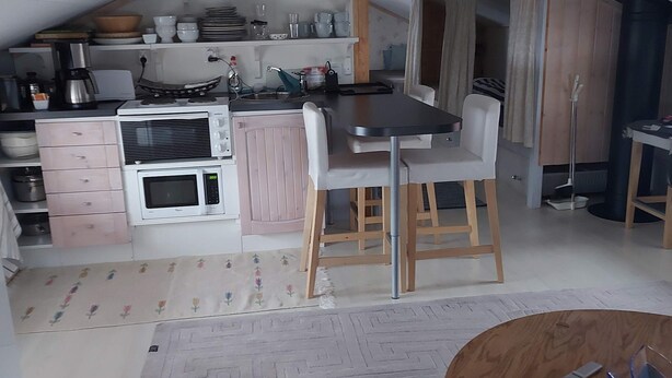 A compact kitchen with a microwave, stove, and bar stools. - 7 Person Holiday Home in Grisslehamn (Grisslehamn)