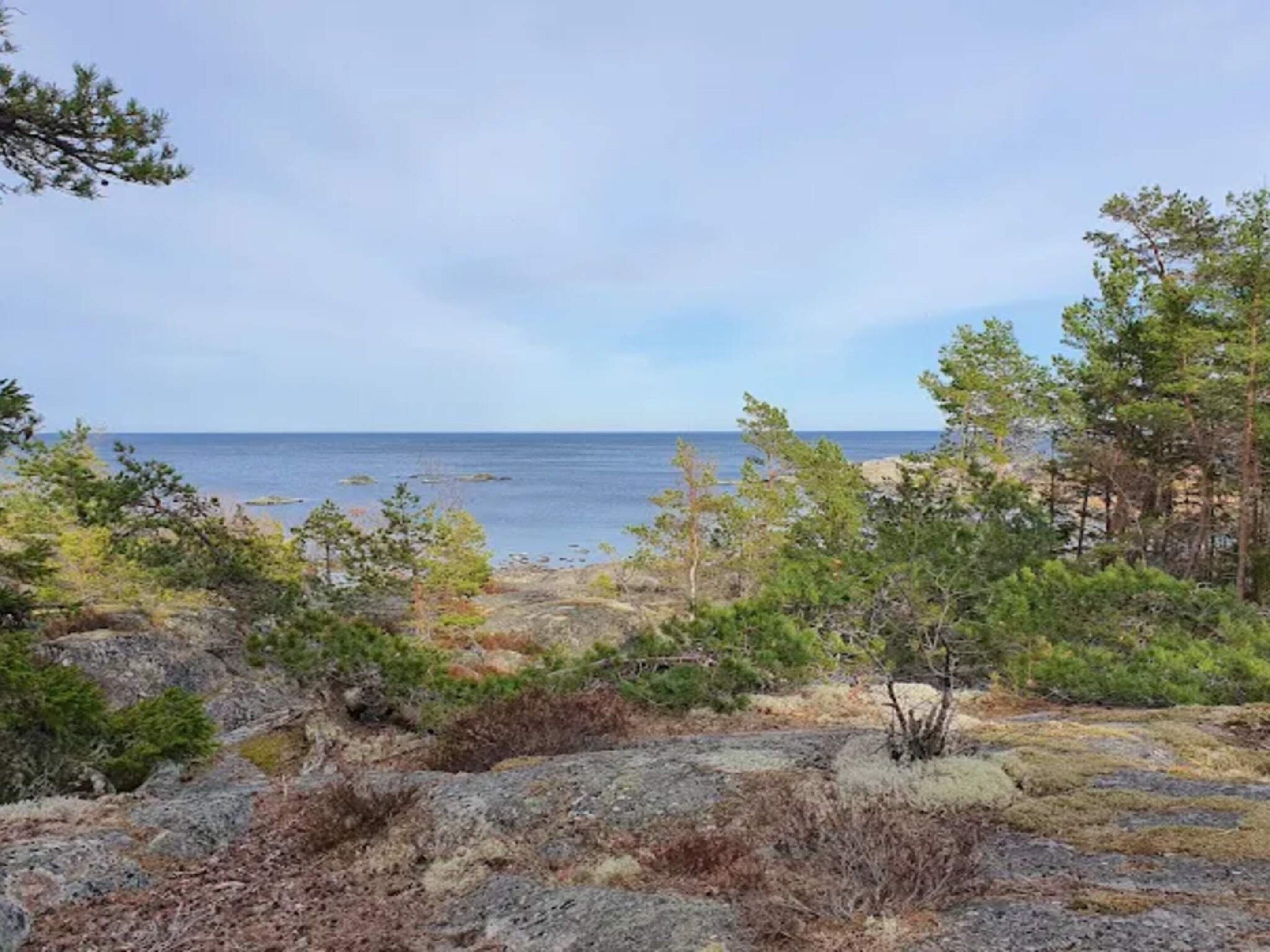 A coastal landscape with rocky terrain and sparse vegetation, leading to a view of the sea.