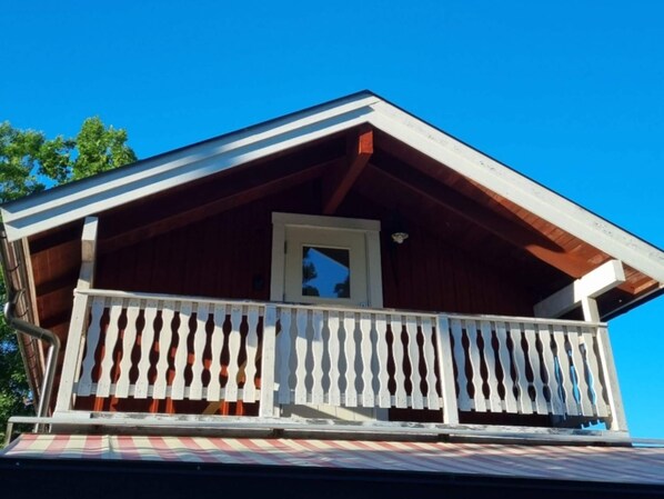 A wooden cabin with a balcony, a window, and a door. - 7 Person Holiday Home in Grisslehamn (Grisslehamn)