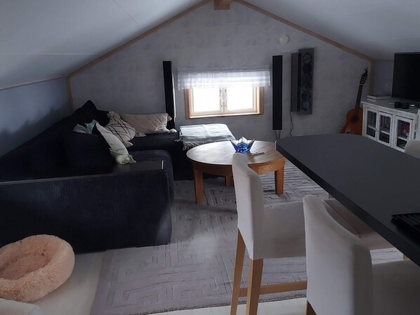 A cozy attic room with a dark-colored sofa, a small round table, and a white chair. - 7 Person Holiday Home in Grisslehamn (Grisslehamn)