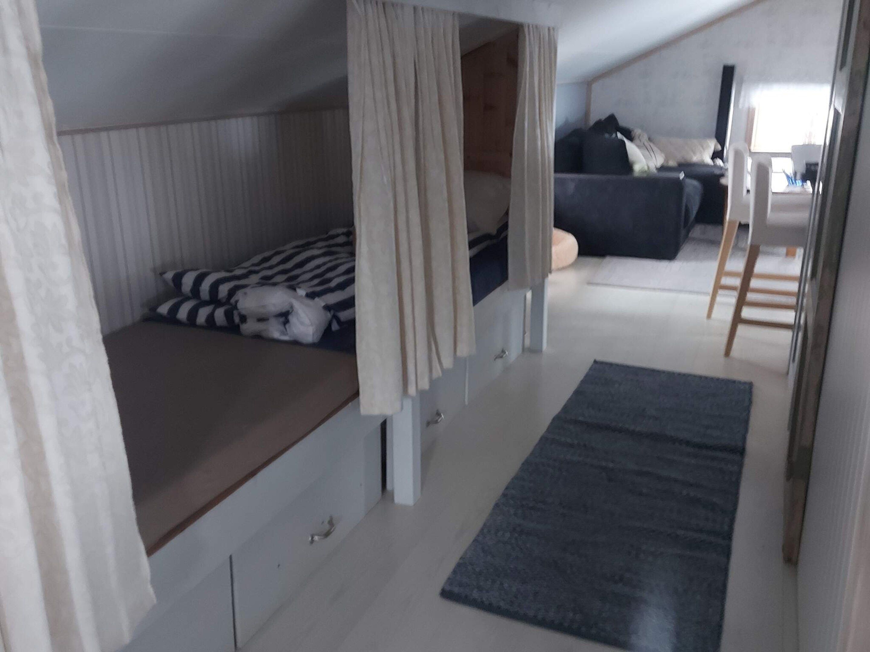 A compact room with a bunk bed, a sofa, a small table, and a ladder.