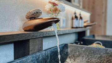 A water feature with a stone basin and a wooden shelf with bottles.