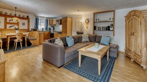 A spacious living area with a sofa, a dining table, and a kitchen in the background. - Waldhaus Sonnenberg Apartment 1 (Drachselsried)