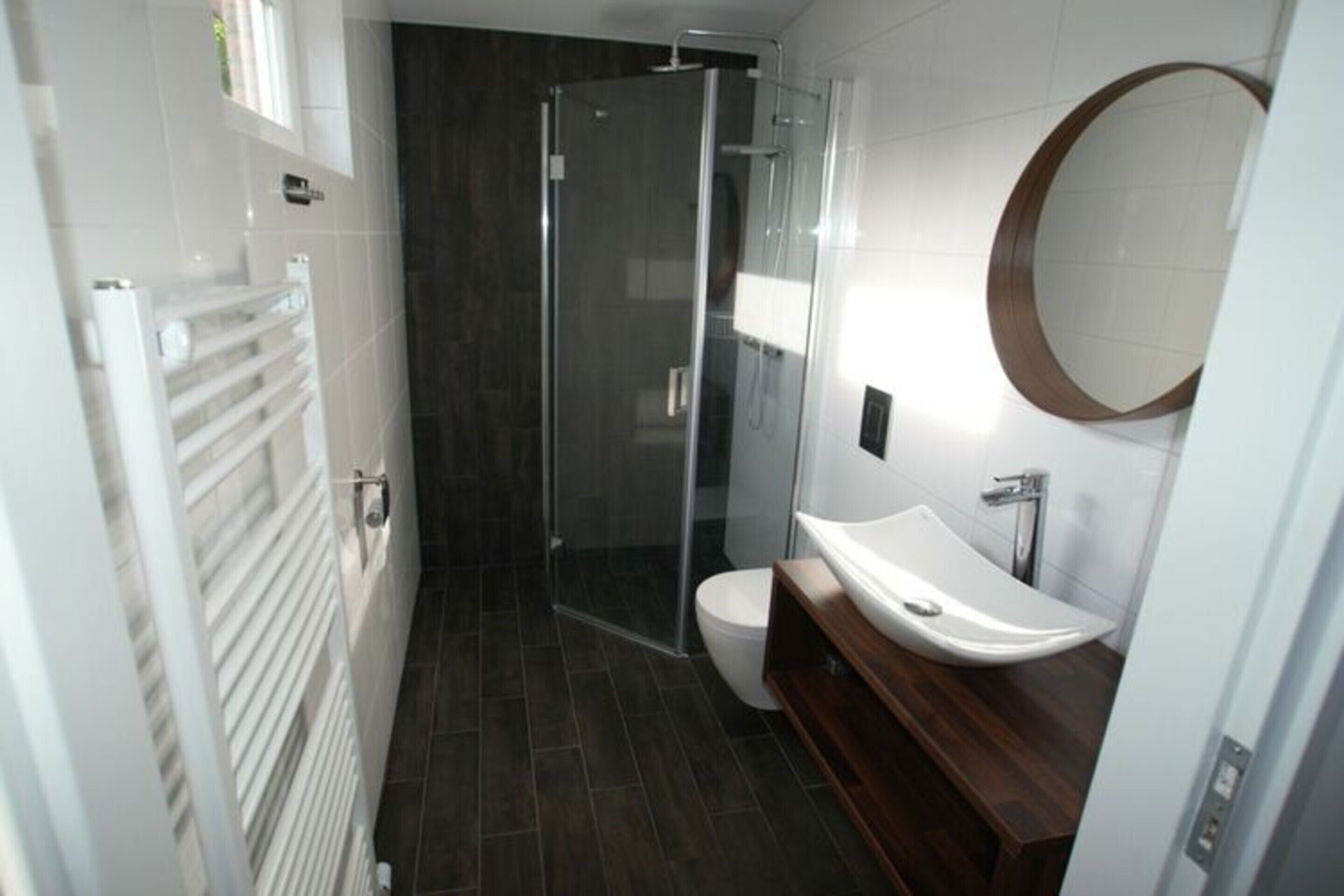 Un bany modern amb box dutxa de vidre, un vàter blanc i un moble de bany de fusta amb un lavabo blanc.