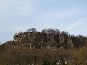 A rocky hill with sparse trees and a few buildings at the base.