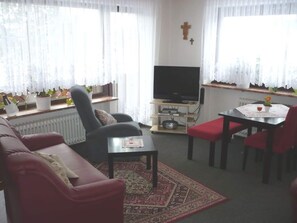 A living room with a sofa, a television, a small table, and a dining area with chairs. - Koferl Modern Retreat (Fichtelberg)