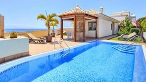 A swimming pool with a pergola and lounge chairs, a small garden, and a view of the sea. - Belvilla by OYO Holiday Home in Puerto de Santiago (Santiago del Teide)