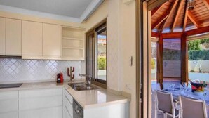A modern kitchen with white cabinets, a built-in dishwasher, and a large window. - Belvilla by OYO Holiday Home in Puerto de Santiago (Santiago del Teide)
