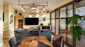 A modern living room with a wooden dining table, grey sofas, and a large TV. - Mosel Sky Lounge With Loggia & Panoramic View (Kenn)