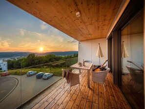 Una terraza de madera con una mesa, sillas, una guitarra y vistas del atardecer sobre un paisaje.