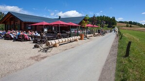 A rustic outdoor dining area with wooden tables and red umbrellas, surrounded by a gravel path and a wooden fence. - Attractive Apartment in Diemelsee (Diemelsee)