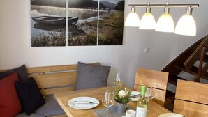 A dining area with a wooden table set for two, a bench with cushions, and a large landscape painting above. - Attractive Apartment in Diemelsee (Diemelsee)
