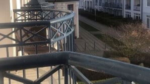 A balcony with a metal railing overlooking a street with traditional buildings. - Holiday Apartment With the Sound of the sea (Kuehlungsborn)