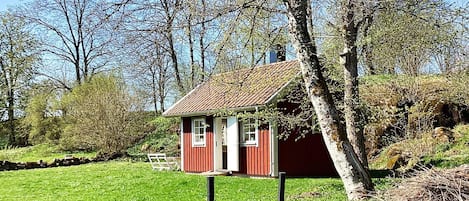 A small red wooden house with a sloped roof, surrounded by a grassy area and trees.