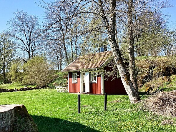 A small red wooden house with a sloped roof, surrounded by a grassy area and trees.