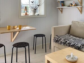A modern living room with a sofa, a wooden table, two black stools, and a window with a view.