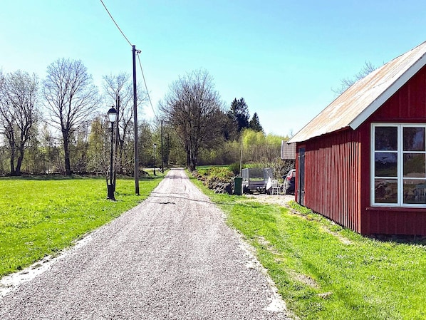 A gravel road leading to a red building with a window, surrounded by green grass and trees. - 4 Person Holiday Home in Falkoping (Falkoping)
