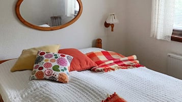 A bedroom with a bed, pillows, a blanket, a mirror, and a wall-mounted light fixture.