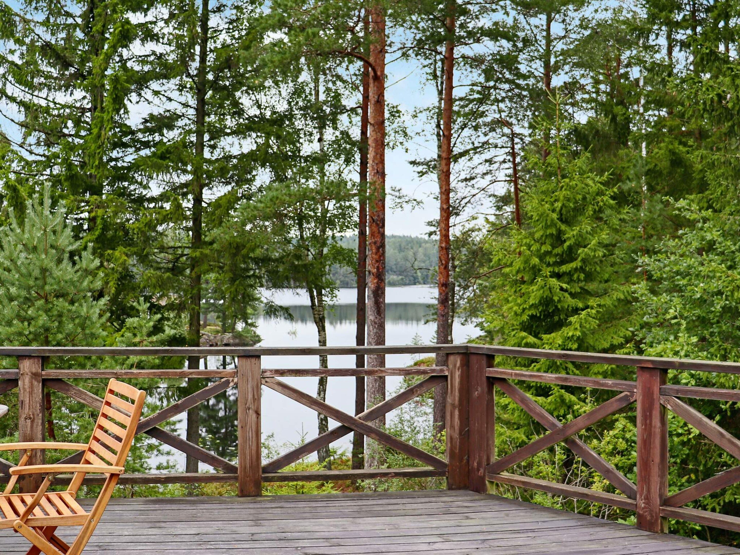 A wooden deck with a wooden chair, overlooking a lake surrounded by trees.