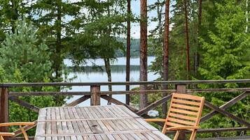 A wooden deck with a table and two chairs, overlooking a lake surrounded by trees.
