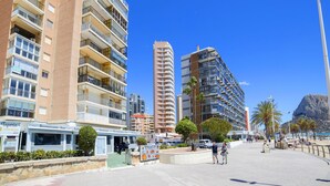 Una zona costiera urbana con edifici a più piani, un marciapiede lastricato e una spiaggia sullo sfondo.
