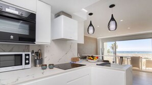 Una cucina moderna con forno a microonde, fornello e forno integrati. C'è un piano di lavoro in marmo, una ciotola di frutta e vista sull'oceano attraverso ampie finestre.