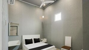 Un dormitorio moderno con una cama grande, una mesita de noche, una silla, un ventilador de techo y un ventanal pequeño.