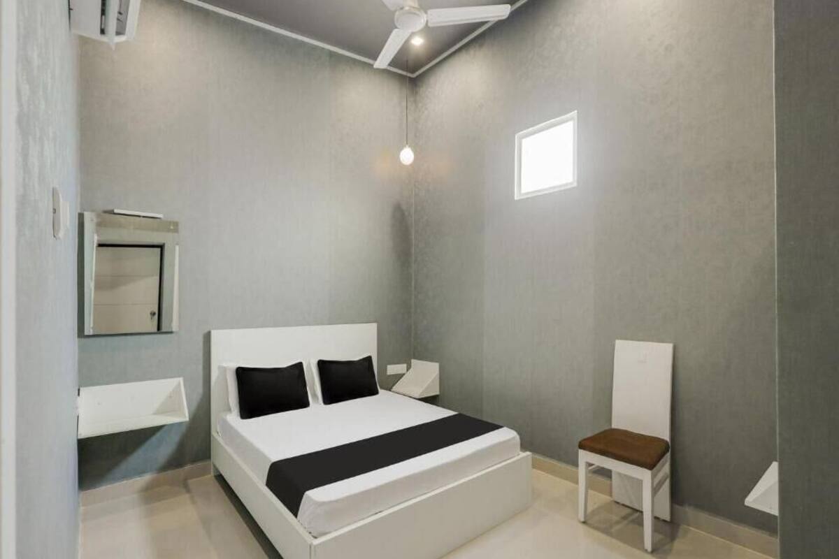 Een moderne slaapkamer met een groot bed, een nachtkastje, een stoel, een plafondventilator en een klein raam.