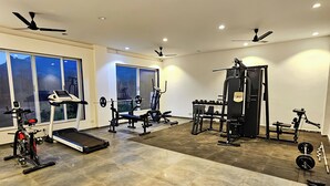 Et rummeligt fitnessrum med forskellig træningsudstyr, store vinduer og ventilatorer i loftet.