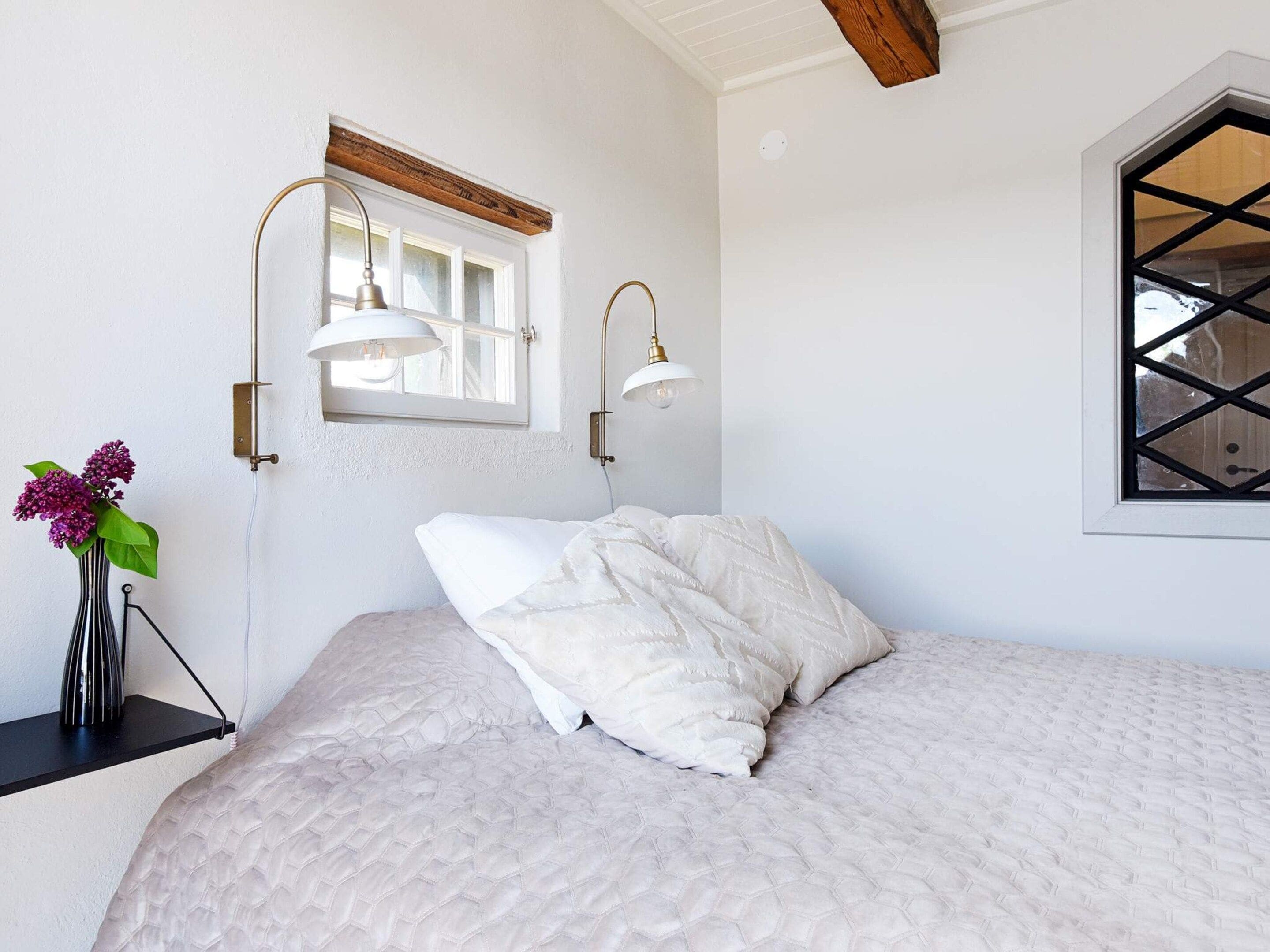 A bedroom with a bed, a window with a view, and wall-mounted lamps.