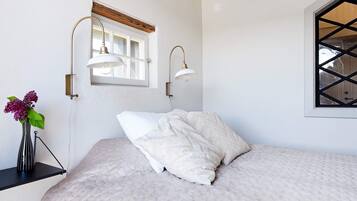 A bedroom with a bed, a window with a view, and wall-mounted lamps.