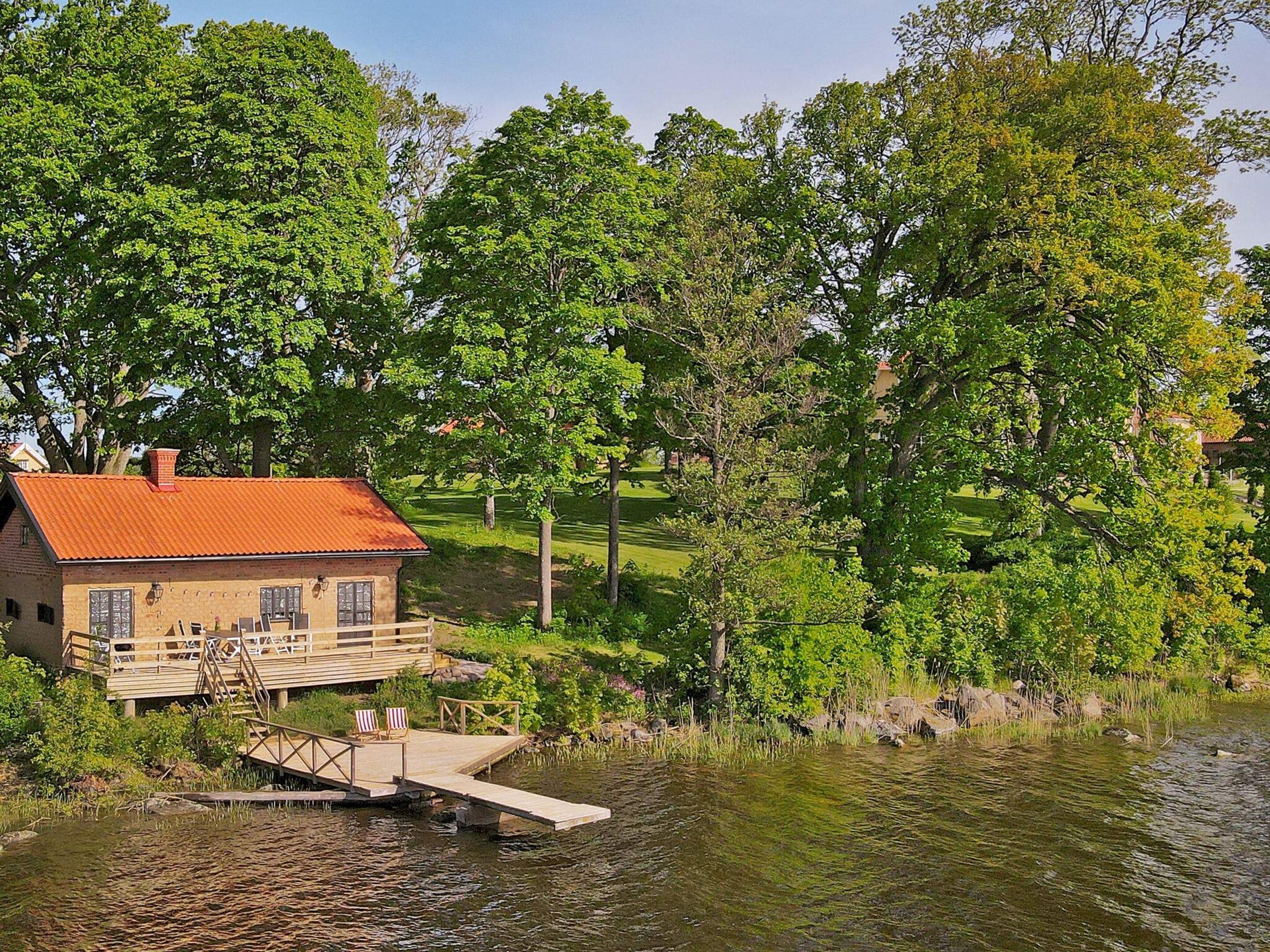 A lakeside cabin with a dock and chairs, surrounded by lush greenery and trees.