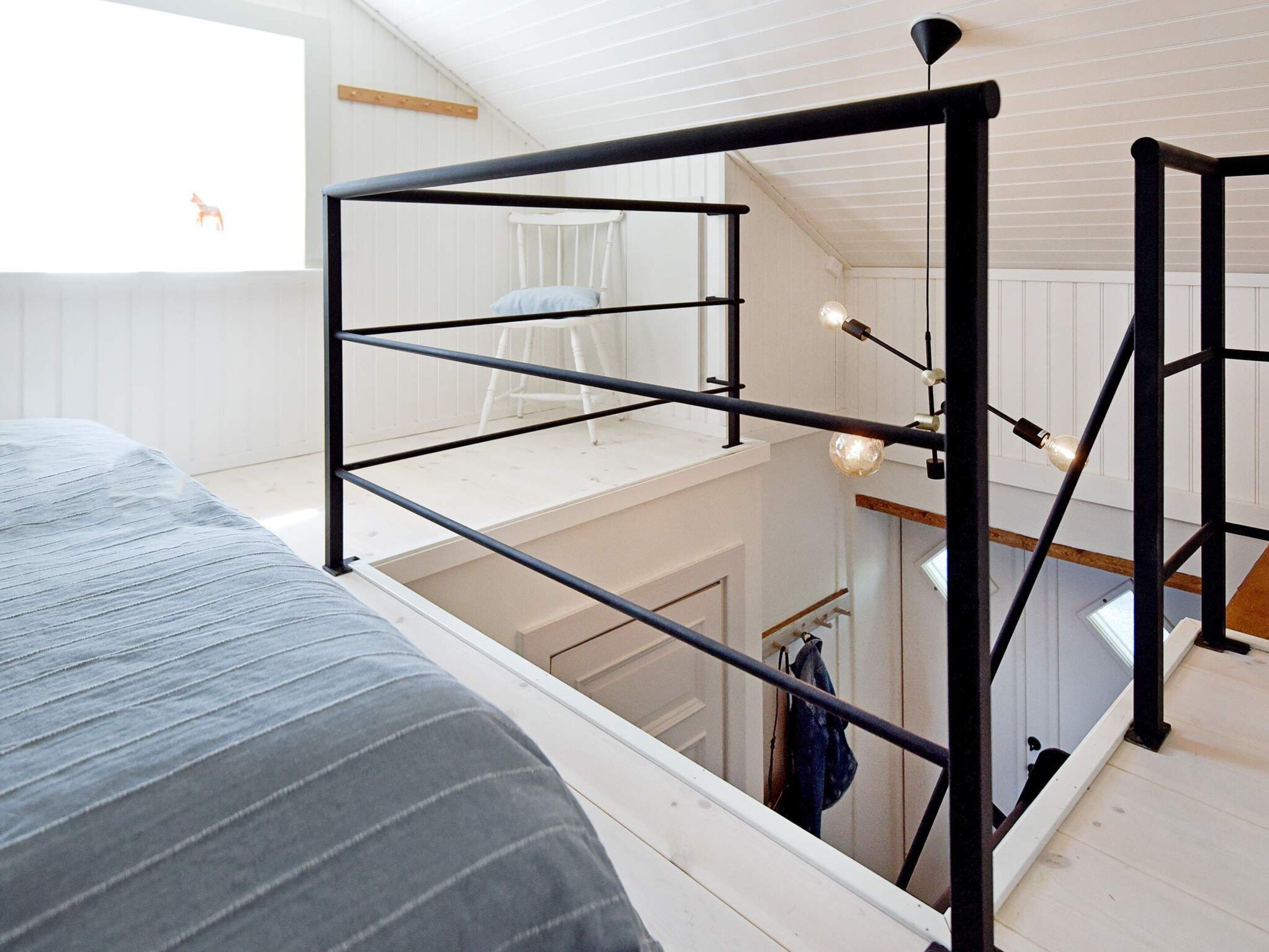 Un lit superposé avec une structure en métal, un mur blanc et une fenêtre donnant sur une chaise blanche à l’extérieur.