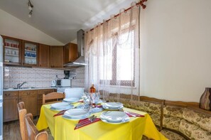 A dining area with a yellow tablecloth, wooden chairs, and a window with lace curtains. - Sunce Comfortable Holiday Residence (Pula)