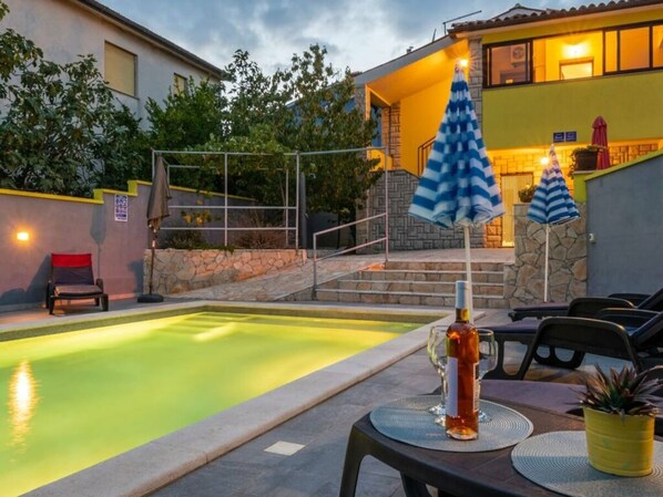 Une piscine avec un mur en pierre et une chaise. On y trouve une table avec une bouteille et des verres.