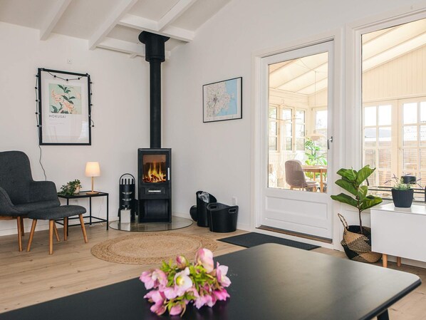 A room with a wood-burning stove, a dining area, and a view through a glass door. - 6 Person Holiday Home in Haderslev (Haderslev)