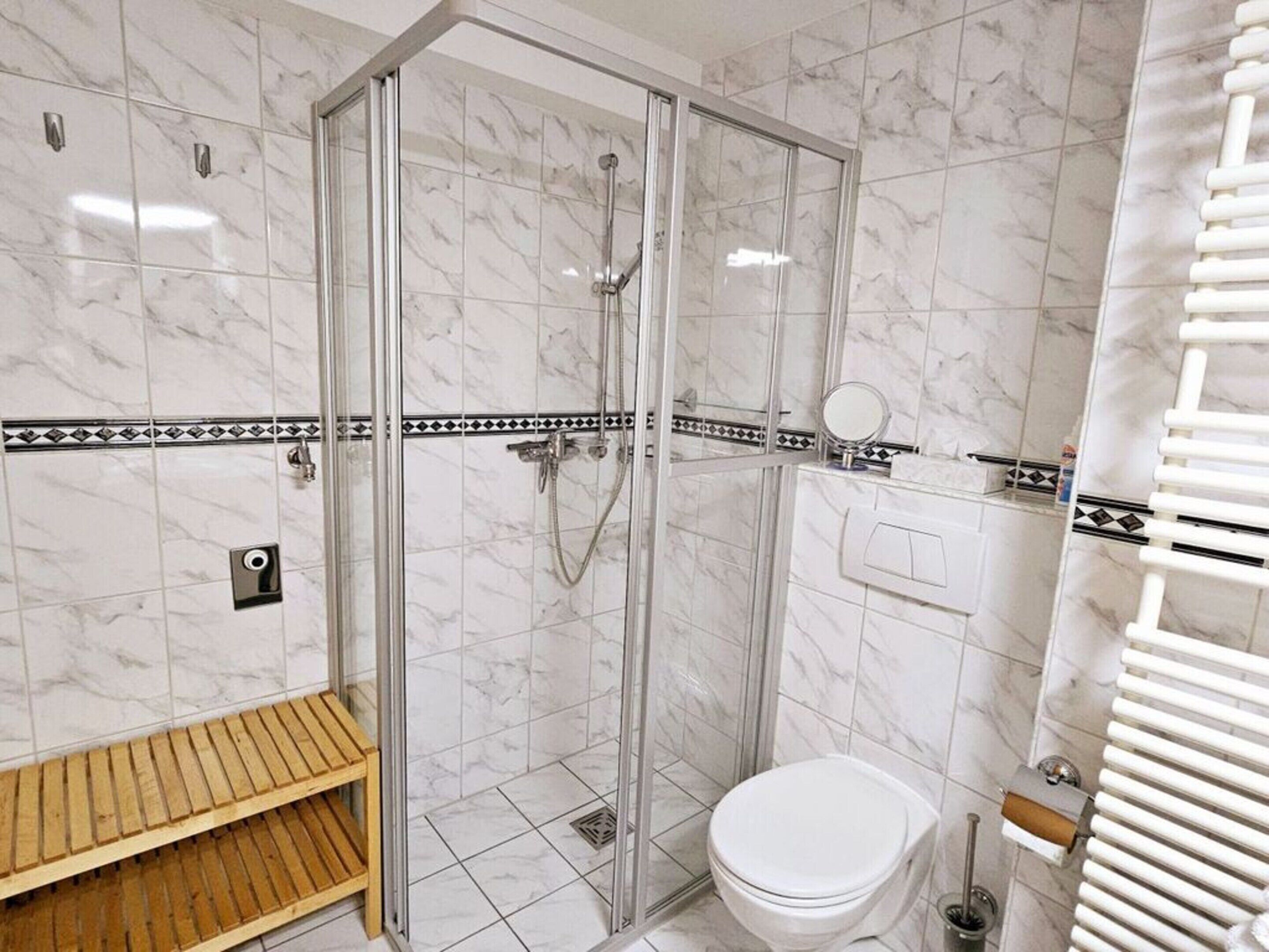 A bathroom with a glass-enclosed shower, a toilet, and a wooden bench.