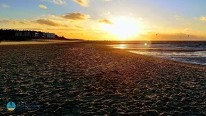 A beach with a sunset, sand, and a distant shoreline with buildings. - Heidhohn Comfortable Holiday Residence (Cuxhaven)