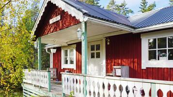 A red wooden house with a white porch and a blue roof.
