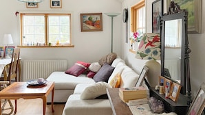 A cozy living room with a sofa, a table, and a mirror. There are windows with curtains, a radiator, and wall-mounted pictures. - 4 Star Holiday Home in Vaddo-by Traum (Väddö)