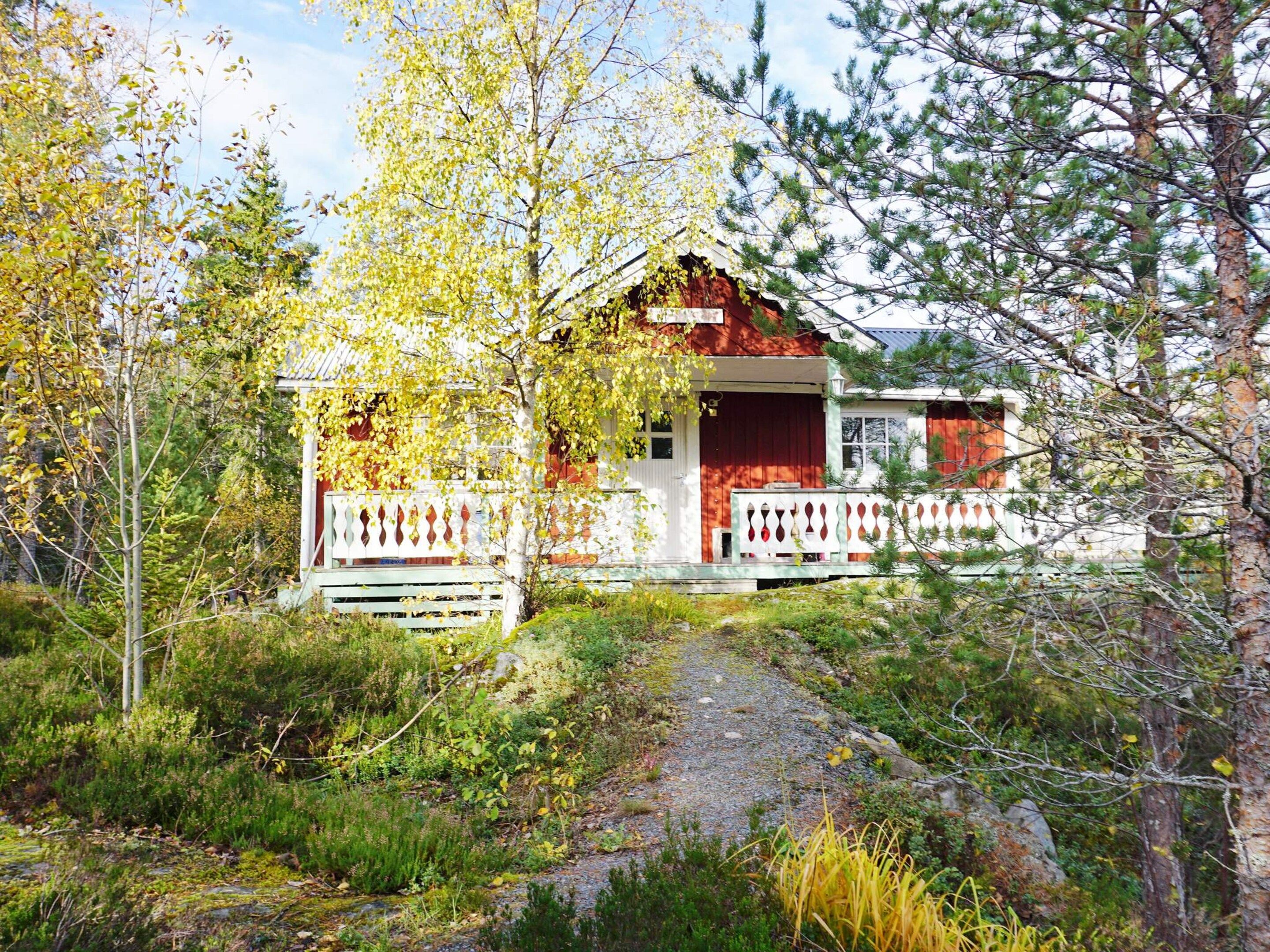A rustic cabin with a porch, surrounded by trees and a gravel path.